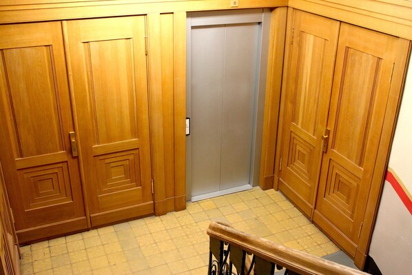 A corner of a room with wooden double doors, a grey elevator, and a tiled floor. - Brivibas Center 2-bedroom apartment (Rīga)