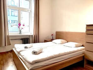Uma cama bem arrumada com lençóis brancos, cabeceira de madeira e mesa de cabeceira com abajur.