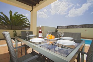 Enjoy a casual meal at this poolside dining area, surrounded by wicker chairs and a glass table.
