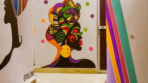 A staircase with a colorful mural on the wall, a door with a handle, and a striped wall on the right. - Mad Squad Hostel (Varanasi)