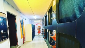 A hallway with lockers, a mural, and a door leading to a bathroom. - Mad Squad Hostel (Varanasi)