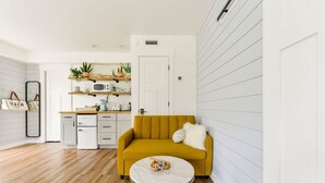 A modern living room with a mustard yellow sofa, a white coffee table, and a kitchen area with white cabinetry and a microwave. - Pet friendly studio apartment. Minimal shedding dogs only.1 dog max.$25 pet fee (Kill Devil Hills)