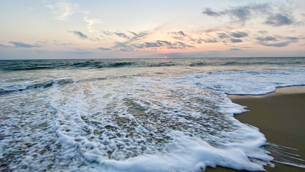 A beach with waves approaching the shore, a clear sky, and a sunset in the distance. - Pet friendly studio apartment. Minimal shedding dogs only.1 dog max.$25 pet fee (Kill Devil Hills)