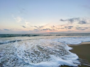 A beach with waves approaching the shore, a clear sky, and a sunset in the distance. - Pet friendly studio apartment. Minimal shedding dogs only.1 dog max.$25 pet fee (Kill Devil Hills)