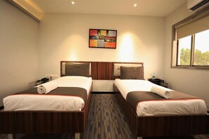 Habitación de hotel con dos camas, cabecera, un cuadro colgado en la pared, una ventana y suelo alfombrado.