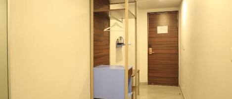 A hallway with a bed, a wooden door, and a mirror on the left wall.