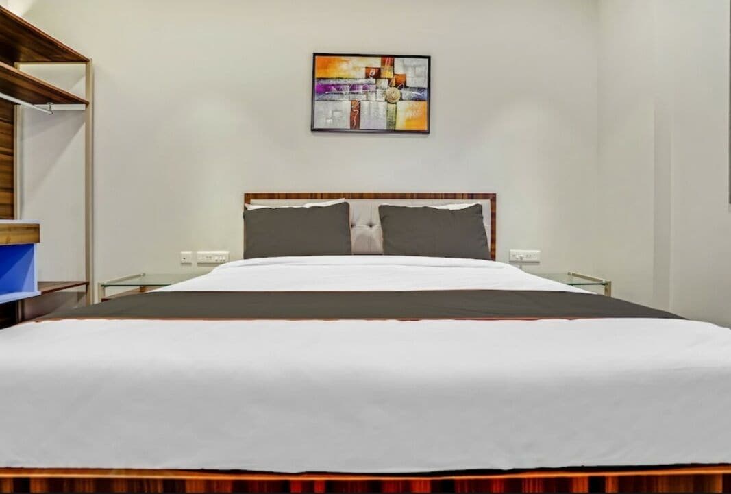 A neatly made bed with a wooden headboard, a wall-mounted abstract painting, and a bedside table with a lamp.