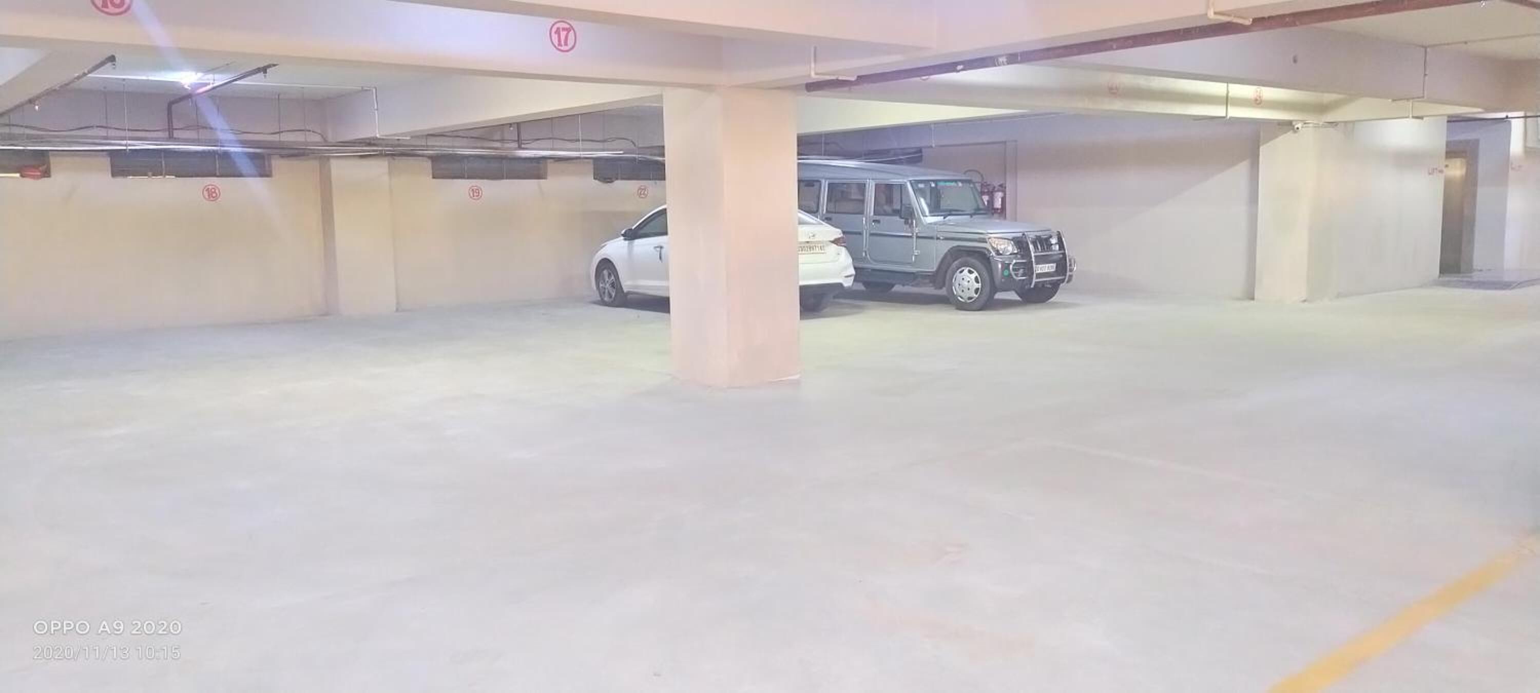 Un estacionamiento con pisos y paredes de concreto, que muestra varios coches estacionados, incluyendo un sedán blanco y un SUV oscuro.