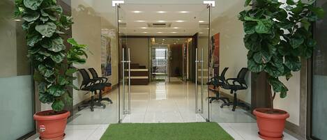 A reception area with a glass door, two potted plants, a green carpet, and office chairs.