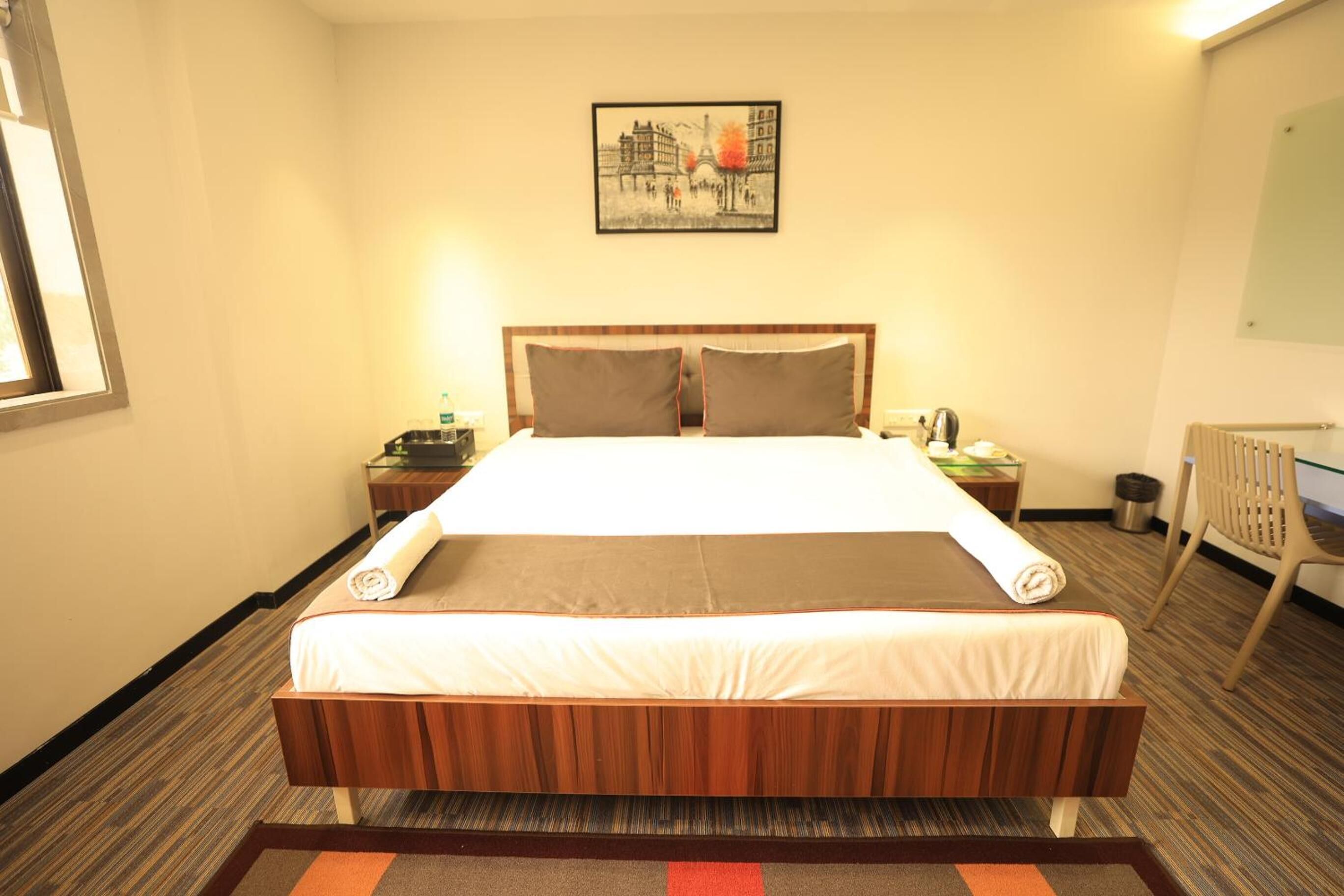 A hotel room with a large bed, a nightstand, a chair, a radiator, and a framed picture on the wall.