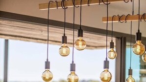 Een eetruimte met een houten tafel en stoelen, hangende lampen en uitzicht op groen.
