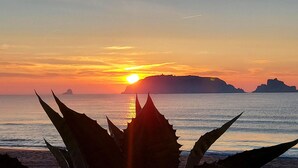 Um pôr do sol sobre uma paisagem costeira com formações rochosas destacadas ao longe.