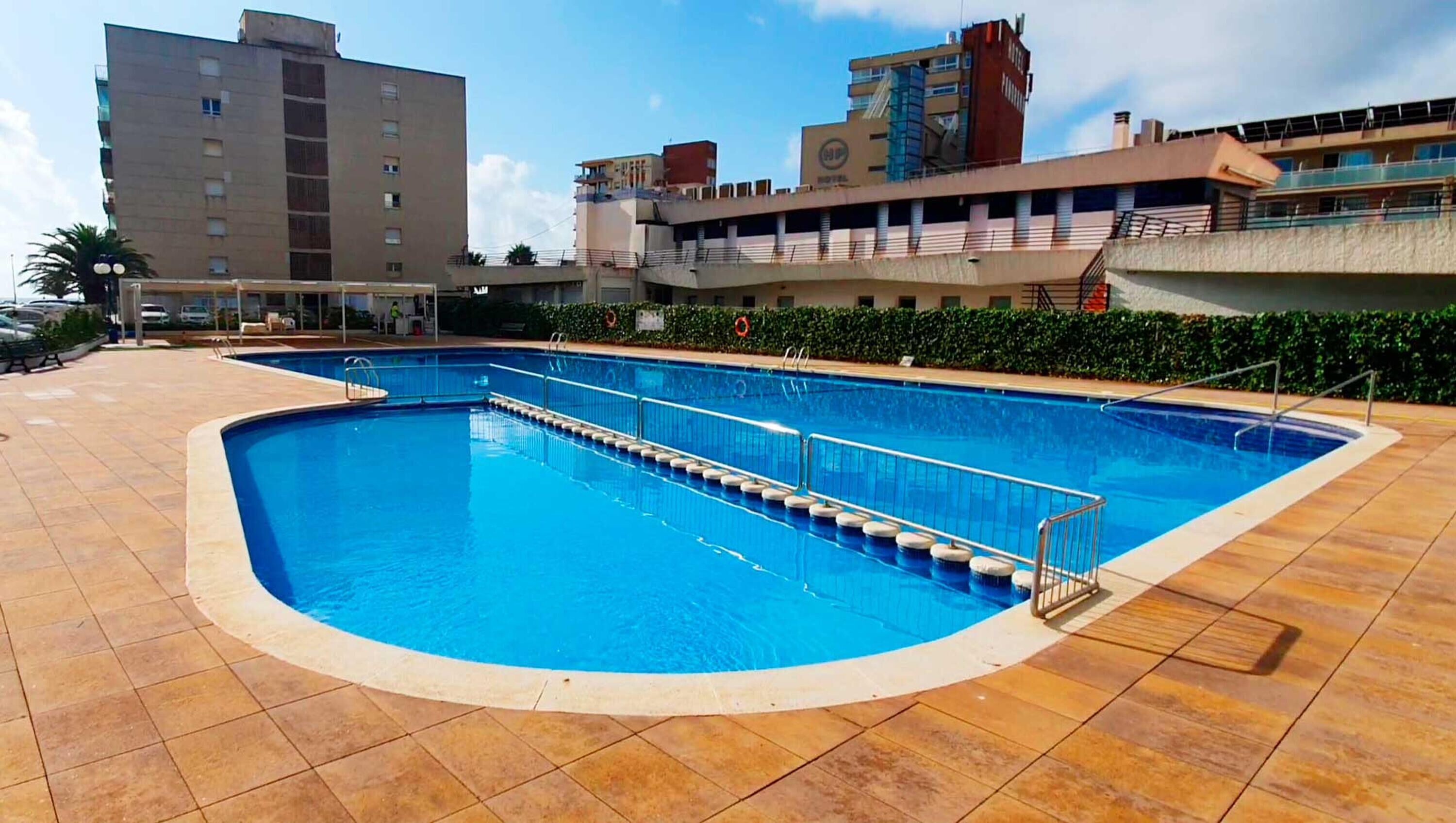 A swimming pool with a tiled deck, surrounded by buildings.