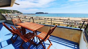 A balcony with a wooden table and chairs overlooking a beach with a parking lot and a distant island. - Rocamaura II-6-9 Apartment to rent in L'Estartit. First line on sea and the beach (Estartit)