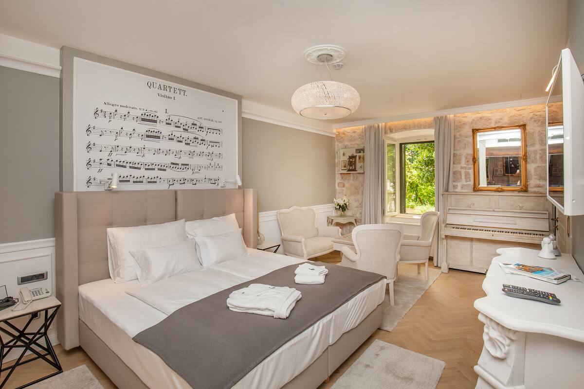 Een slaapkamer met een bed, een piano, een bureau en een groot poster aan de muur.