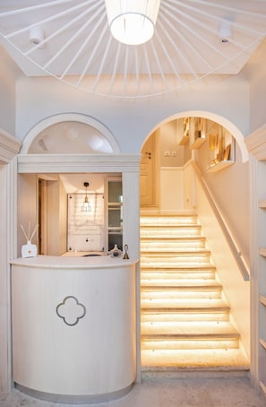Een trap met een modern design, een receptiebalie met een decoratief object, en een plafond met een bijzondere lamp.