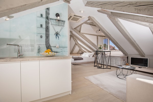 Un dormitorio tipo loft moderno con un tragaluz grande, una cama, un televisor y una zona de cocina con un mural.