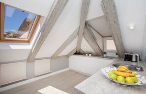 A modern kitchen with exposed wooden beams, a skylight, and a fruit bowl on the counter.