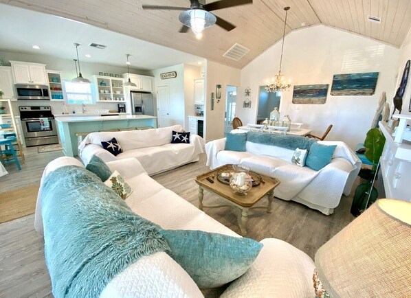 A spacious living area with a large sofa, a coffee table, and a dining area with a chandelier.