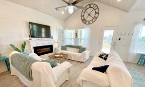 A spacious living room with a fireplace, white sofas, a coffee table, and a television mounted on the wall.