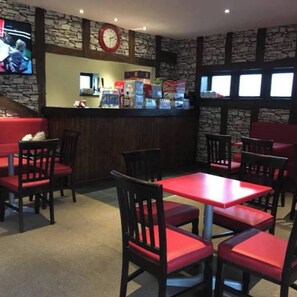 A restaurant interior with stone walls, red cushioned booths, and a bar area.