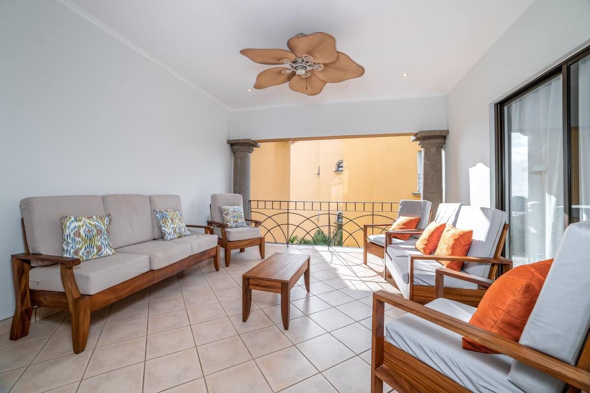 A spacious balcony with a ceiling fan, a sofa, armchairs, and a table, offering a view of the building's interior.