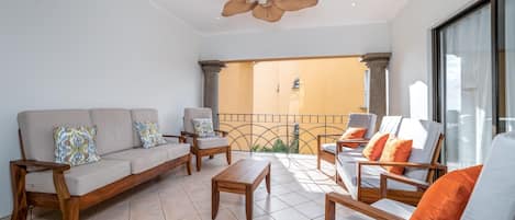 Ein geräumiger Balkon mit Deckenventilator, einer Couch, Sesseln und einem Tisch, der einen Blick ins Innere des Gebäudes bietet.