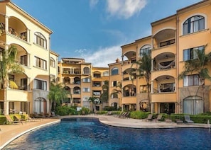 A hotel with a central swimming pool, multiple balconies, and palm trees. - Stay in Tamarindo Condominiums (Tamarindo)
