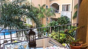 A balcony with a glass table, a bottle, a martini glass, a lantern, magazines, and potted plants. - Stay in Tamarindo Condominiums (Tamarindo)