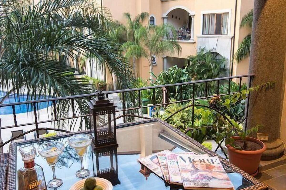 A balcony with a glass table, a bottle, a martini glass, a lantern, magazines, and potted plants.