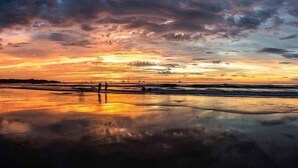 A beach scene with a sunset, calm waters, and a few people walking. - Stay in Tamarindo Condominiums (Tamarindo)