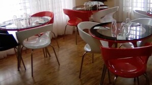 Un comedor con mesas y sillas redondas, cortinas blancas y un equipo de aire acondicionado.
