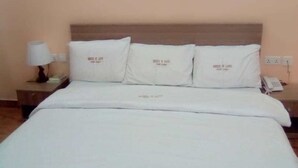 Una cama bien hecha con sábanas y almohadas blancas, una lámpara de noche y un teléfono instalado en la pared.