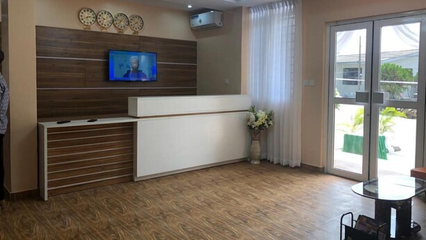 Un área de recepción con un mostrador de madera, un televisor de pantalla plana montado en la pared, una puerta de cristal que da al exterior y una pequeña mesa con un atril para revistas.