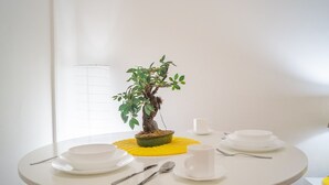 A round dining table with white plates, cups, and cutlery, a yellow placemat, and a bonsai tree centerpiece. - Beautiful 2BR - 12 min from Downtown (Vienna)