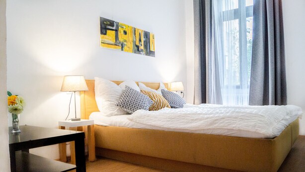 A neatly arranged hotel room with a bed, two bedside tables, a lamp, and a painting on the wall. - Beautiful 2BR - 12 min from Downtown (Vienna)