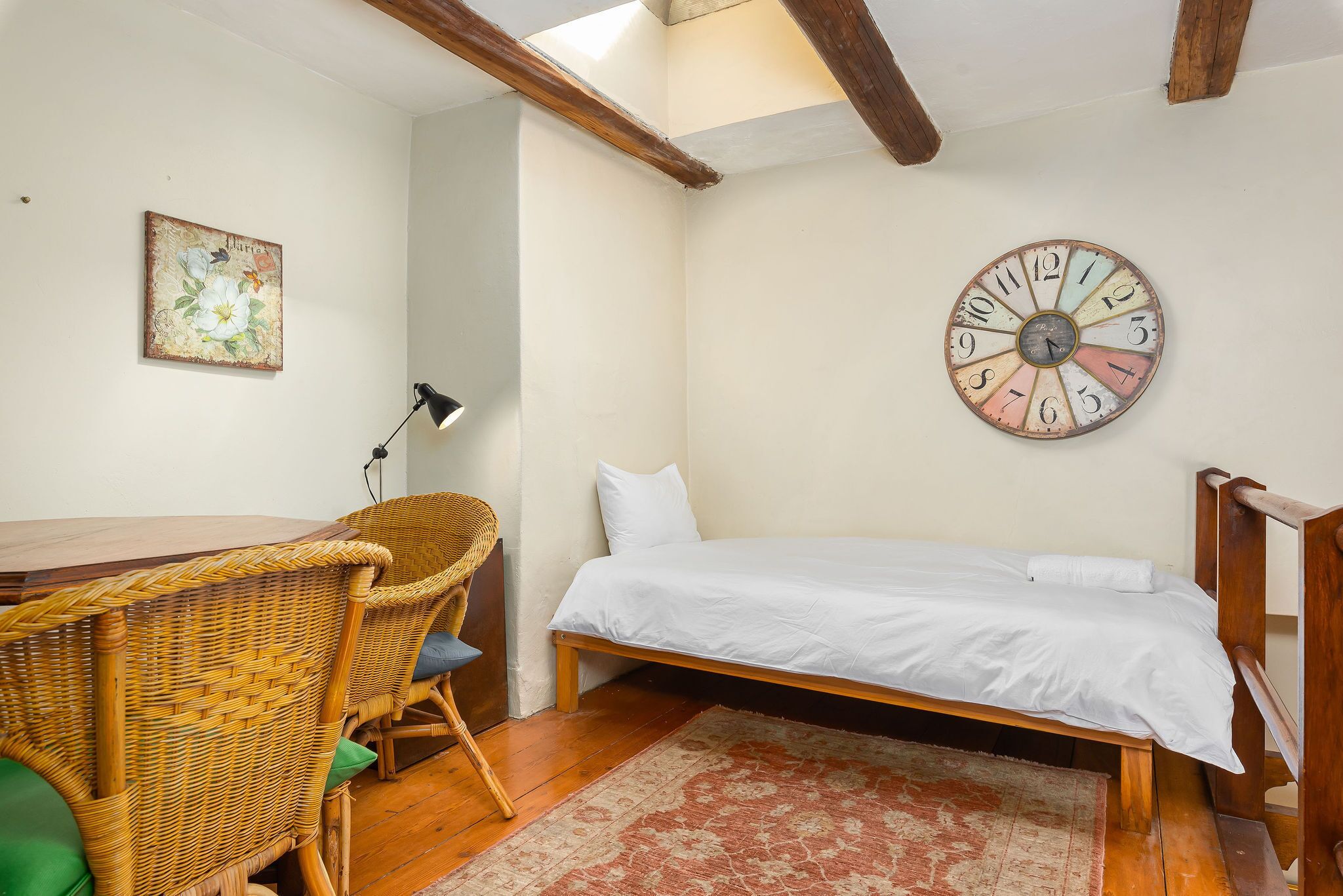 Ein Schlafzimmer mit einem Bett, einem Korbstuhl, einem Schreibtisch und einer Wanduhr.