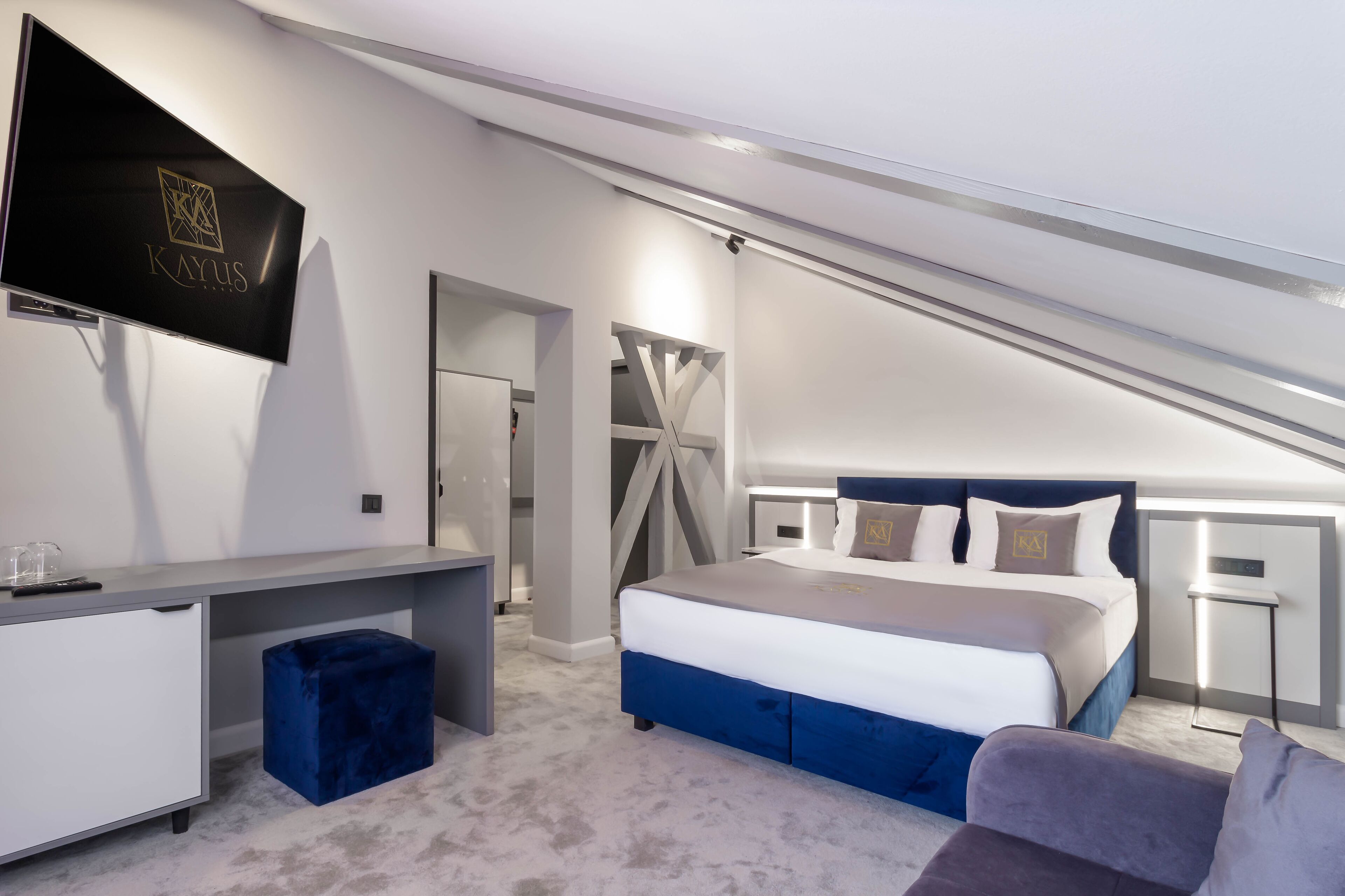 A modern bedroom with a bed, a desk, and a TV mounted on the wall.