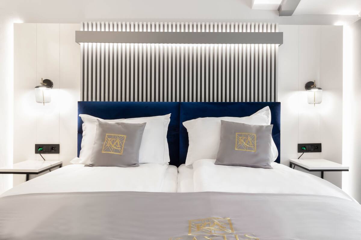A modern hotel room with a large bed, two bedside tables, and a wall-mounted light fixture.