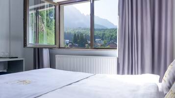A hotel room with a large window offering a view of a forest and mountains.