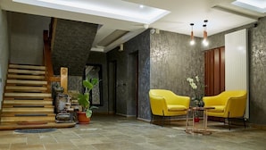 Un intérieur moderne avec un escalier, deux chaises jaunes, une petite table et des plantes en pot.