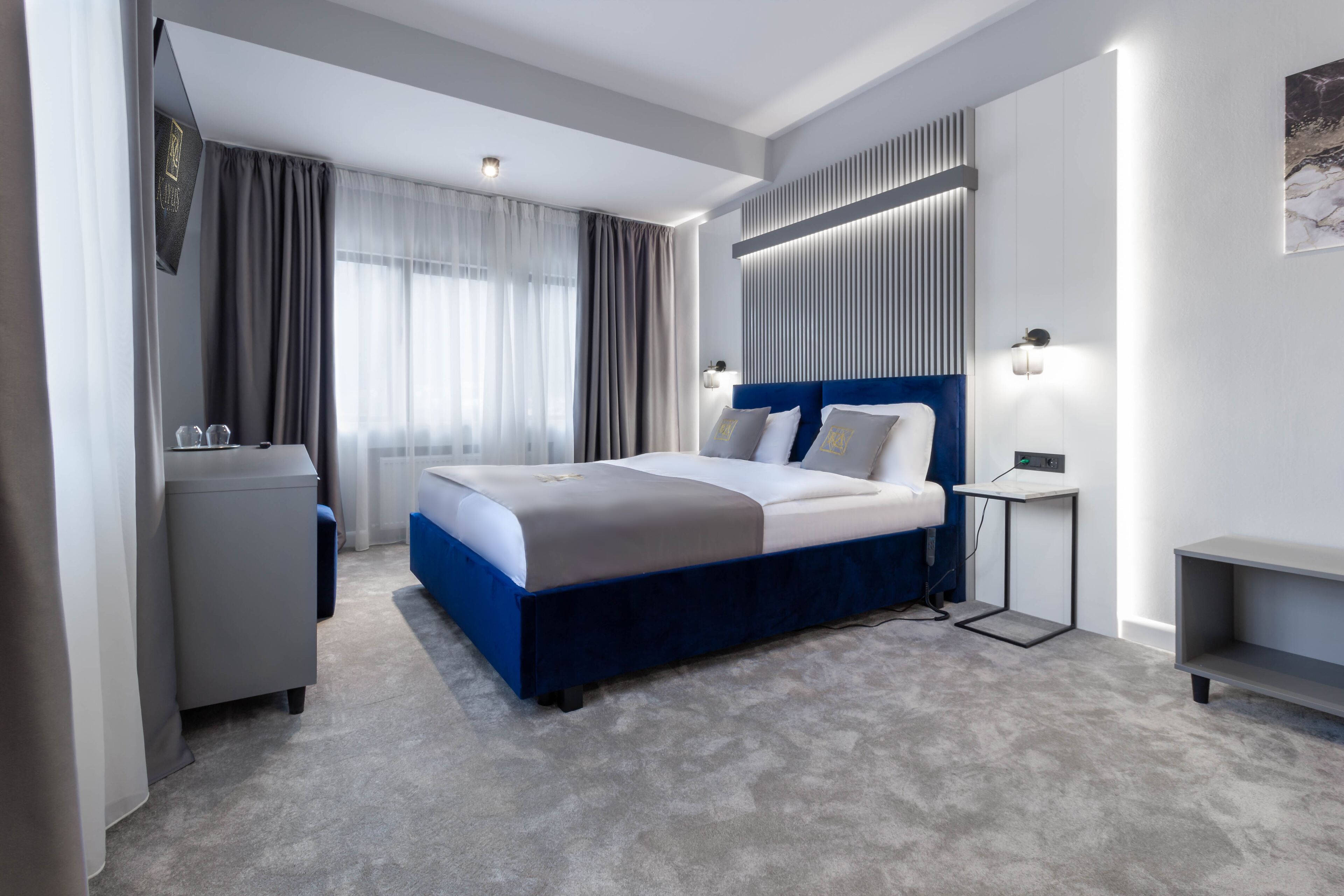 A modern hotel room with a large bed, a desk, and a wardrobe.