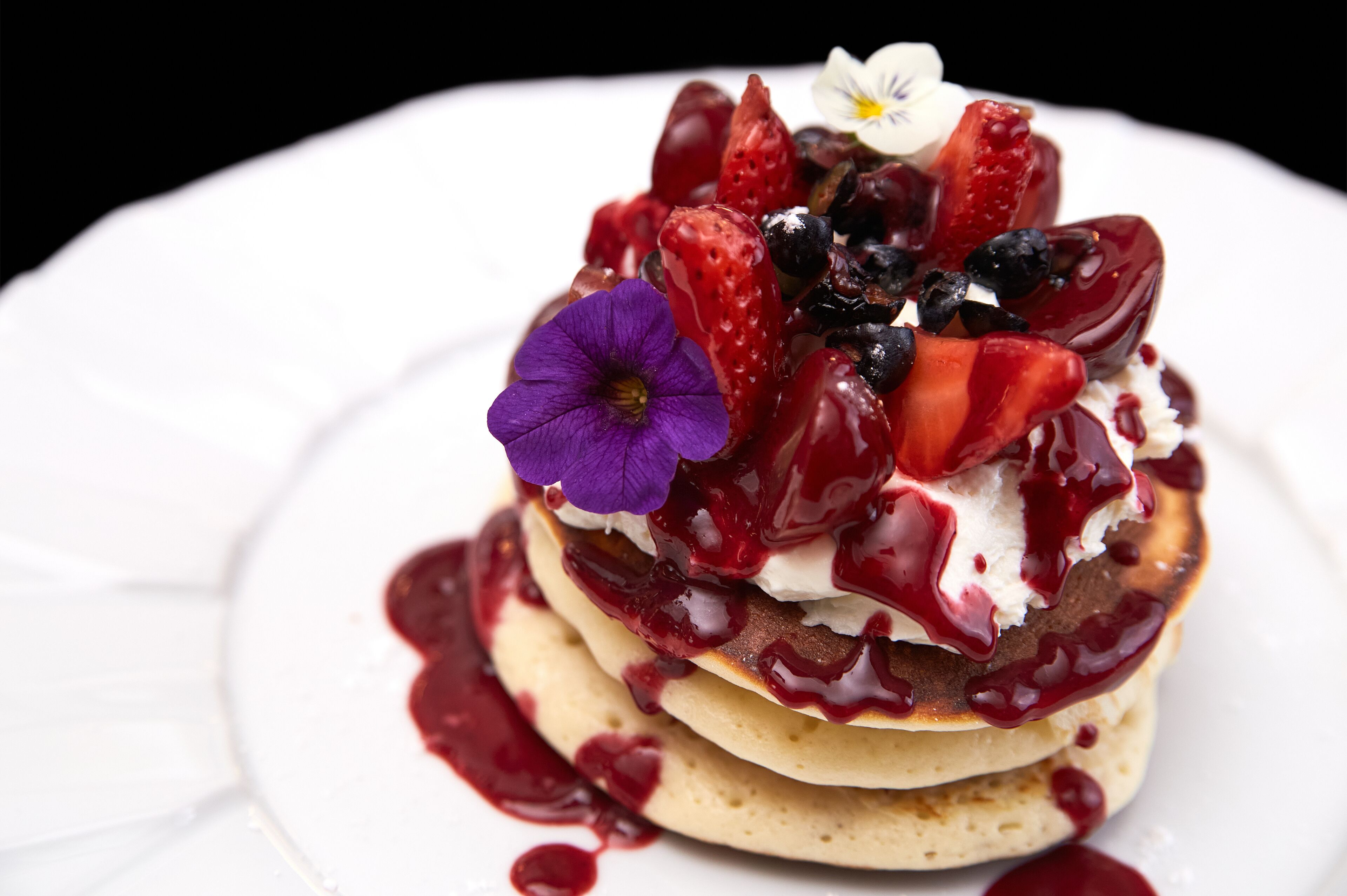 Un postre con fresas, arándanos y una flor morada encima.