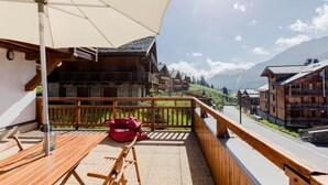 Een houten terras met een tafel, stoelen, een rode tas en een grote parasol.