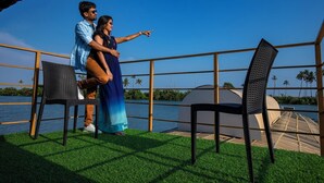 Una pareja parada en una terraza con vista al agua y palmeras.