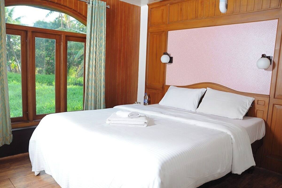 A neatly made bed with white linens, a wooden headboard, and a large window with curtains.