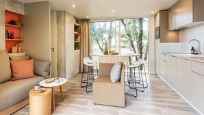Una sala moderna con sofá, una mesa de centro y un comedor con sillas. Se observa una cocina con armarios y un lavamanos.
