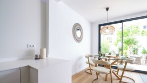 A modern kitchen with a white countertop, a dining area with a glass table and chairs, and a large window with a view of greenery outside. - CITY HOUSE SA FONT IN SANTA CATALINA (Palma)