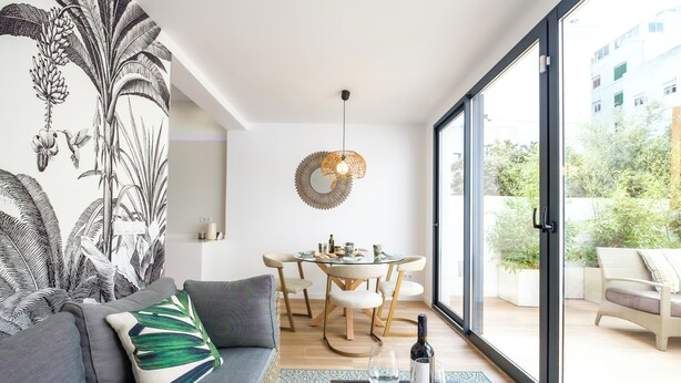 A modern living room with a grey sofa, a round dining table with chairs, a hanging light fixture, and a view of greenery outside. - CITY HOUSE SA FONT IN SANTA CATALINA (Palma)
