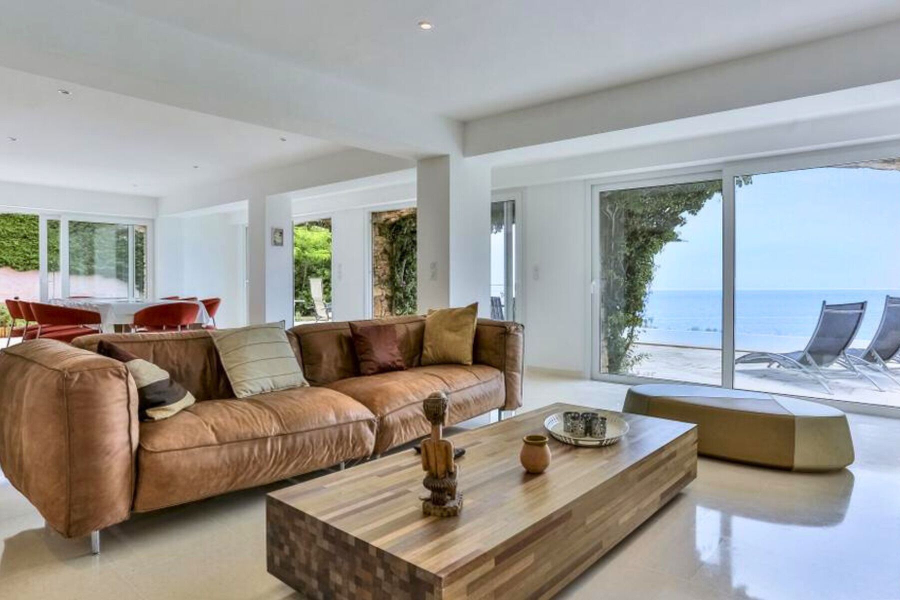 A modern living room with a leather sofa, a wooden coffee table, and a view of the sea through large windows.